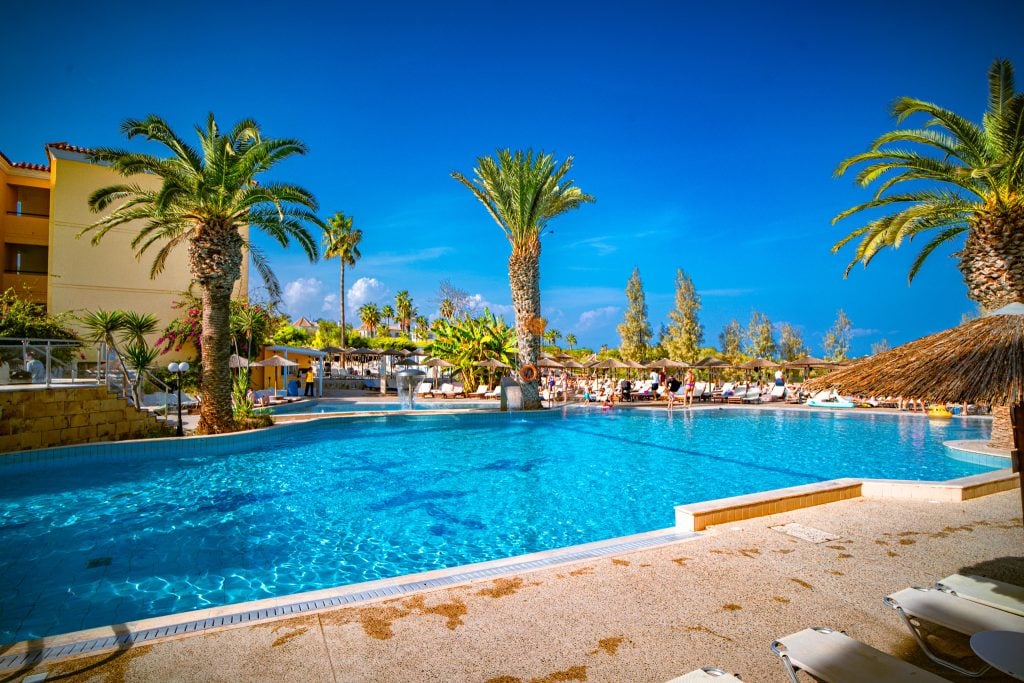 Palm-fringed main pool with sunbeds and thatched parasols at Malama Beach Holiday Village, Protaras