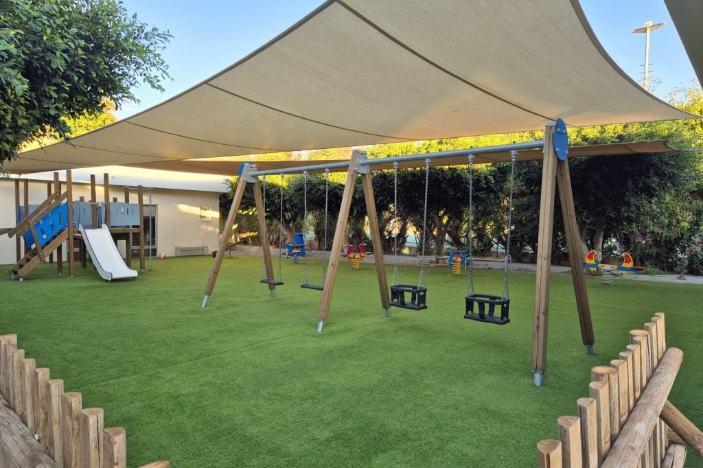 Shaded children's playground with swings and a slide at Malama Beach Holiday Village, Protaras
