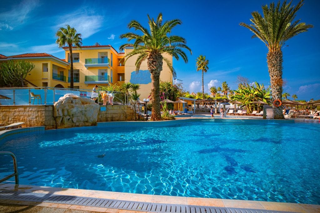 Outdoor pool with a rock feature and palms at Malama Beach Holiday Village, Protaras