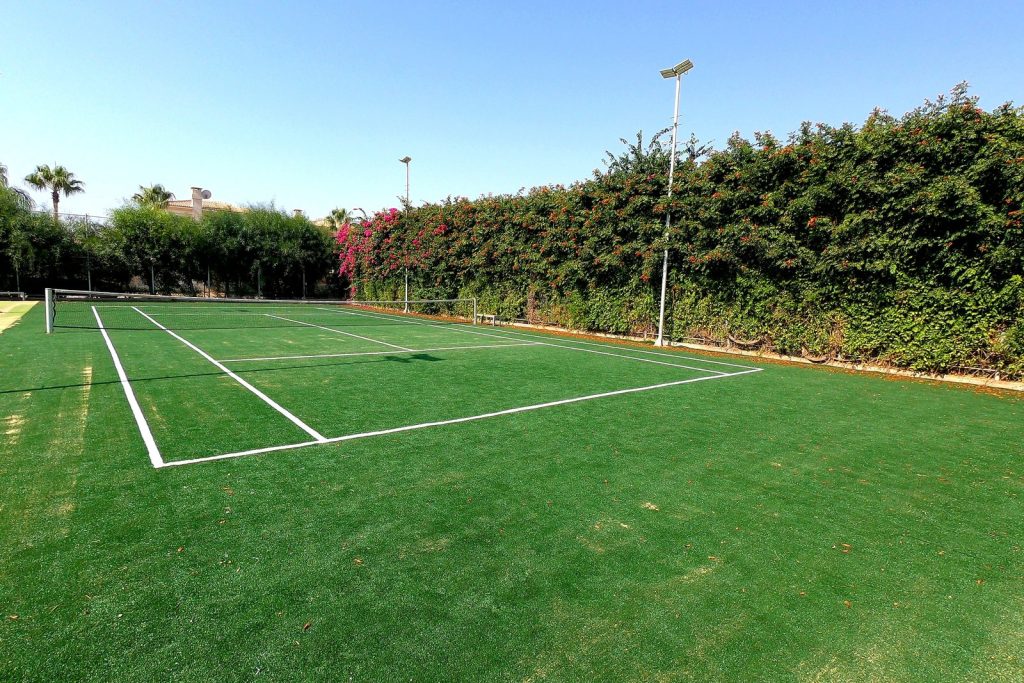 Tennis court surrounded by hedges and gardens at Malama Beach Holiday Village, Protaras